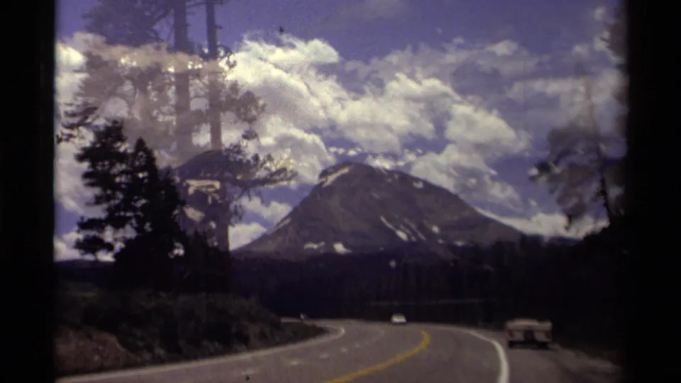 Canadian 8mm travel footage shows a highway approaching a broad mountain peak, with forest silhouettes and cars in the lane.