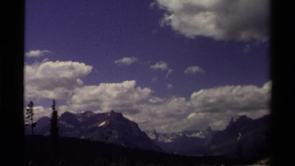 1979 Canadian 8mm still with a mountain ridge, scattered clouds, and dark foreground trees in a soft home-movie exposure.