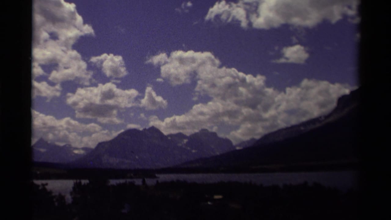 1979 Canadian 8mm frame showing a cloud-filled purple-blue sky above mountain ridges, a lake, and dark tree silhouettes.