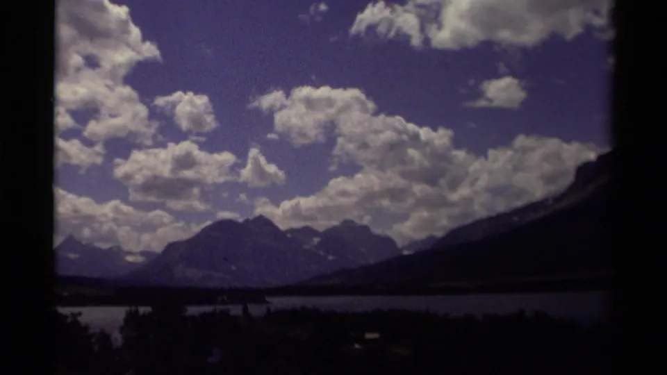1979 Canadian 8mm frame showing a cloud-filled purple-blue sky above mountain ridges, a lake, and dark tree silhouettes.