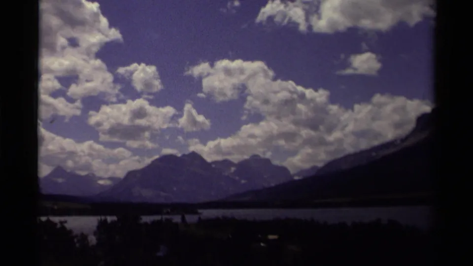1979 Canadian home-movie frame of distant mountains and a lake beneath a broad sky with clustered white clouds.