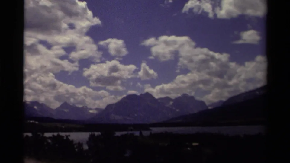 1979 Canadian 8mm view of heavy clouds above shadowed mountain peaks, a lake, and silhouetted trees in the foreground.