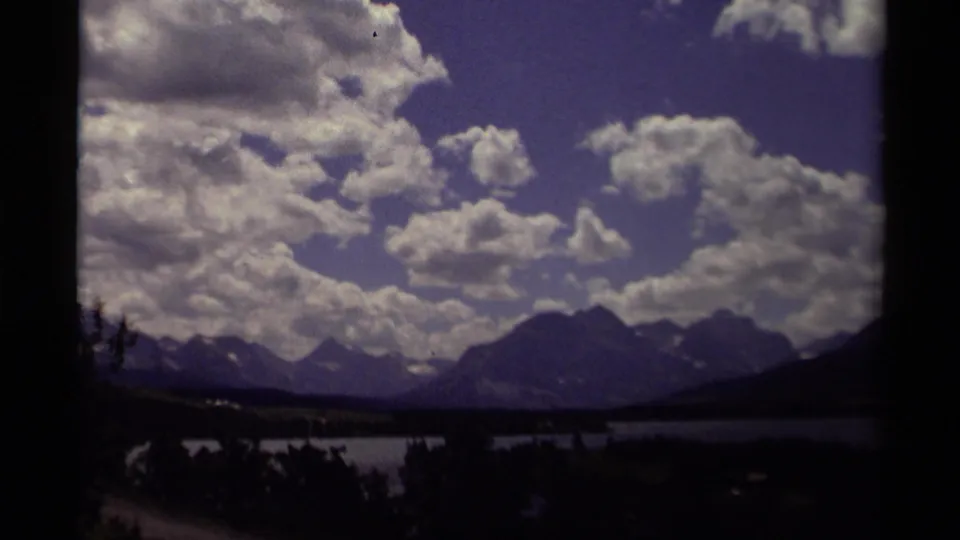 1979 Canadian 8mm view of a lake below distant mountains, with billowing clouds and dark foreground silhouettes.