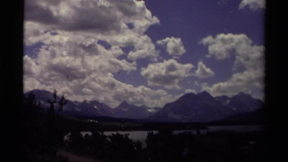 1979 Canadian home-movie frame showing mountains beyond a lake under textured clouds, partly enclosed by dark film-edge shadows.
