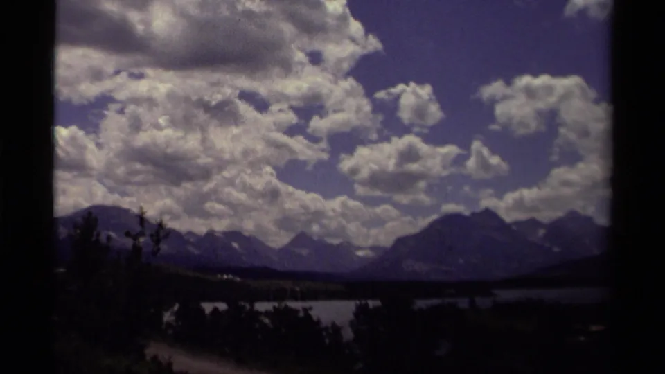 1979 Canadian 8mm frame of a broad lake and mountain horizon under scattered clouds, with foreground shadows and visible film borders.