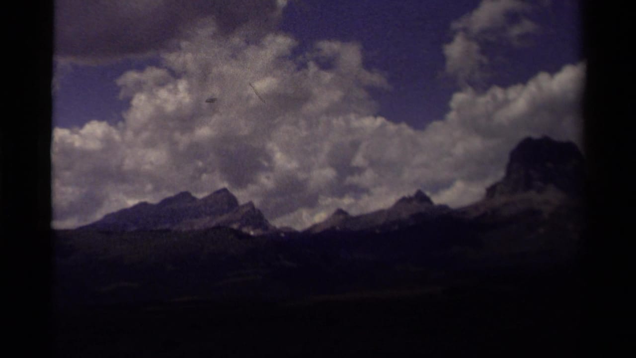 1979 8mm home-movie view of a Canadian mountain range under a cloud-filled sky, framed by dark scan edges.