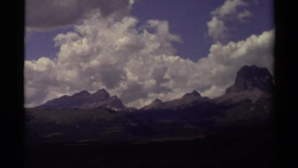 Canadian mountain landscape on 8mm film, with bright cloud cover, distant peaks, rolling hills, and dark gate edges.