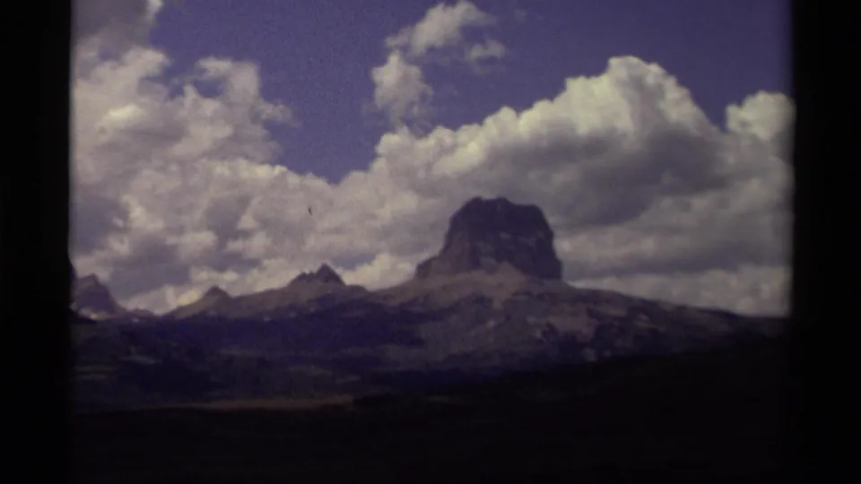 Final 8mm frame of a Canadian mountain peak beneath thick clouds, with ridges, wooded slopes, and visible film edges.