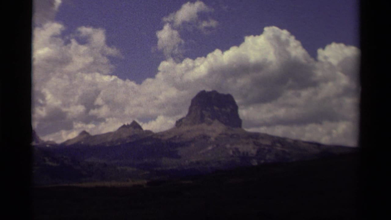 Wide mountain peak under billowing clouds with dark film borders.