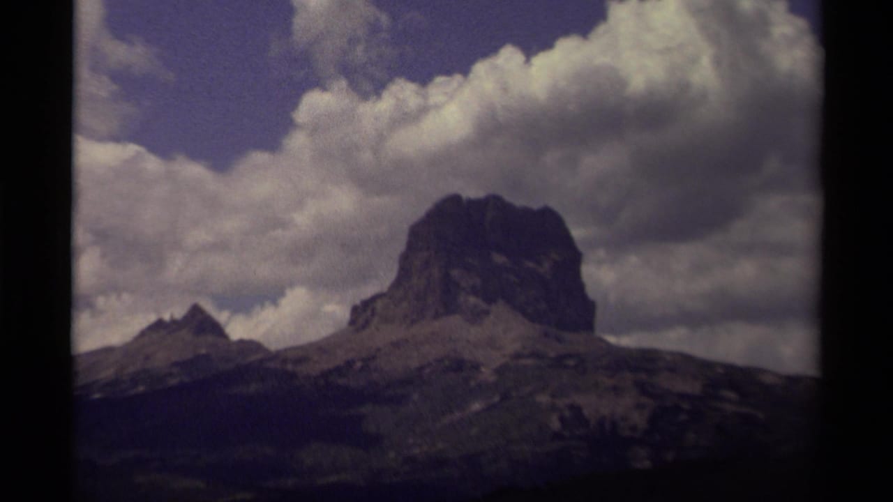 A Canadian mountain landscape on 8mm film, with a broad rocky peak, a smaller pointed summit, and dense clouds overhead.