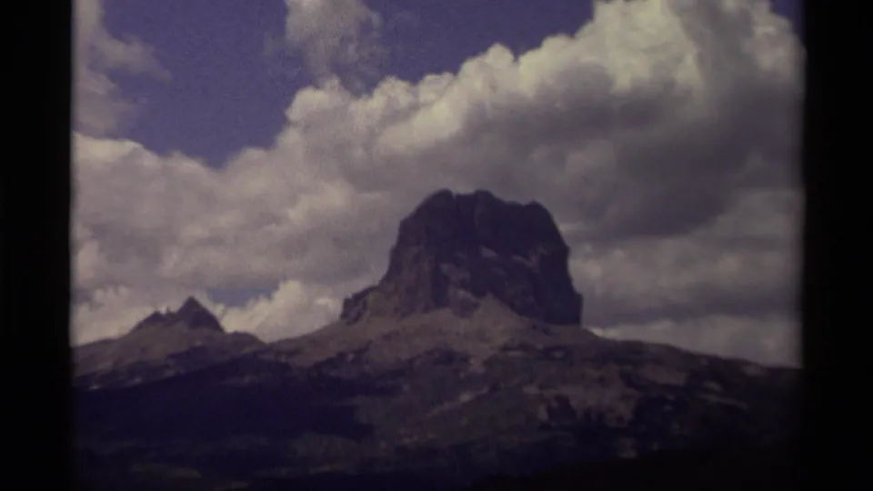 A Canadian mountain landscape on 8mm film, with a broad rocky peak, a smaller pointed summit, and dense clouds overhead.