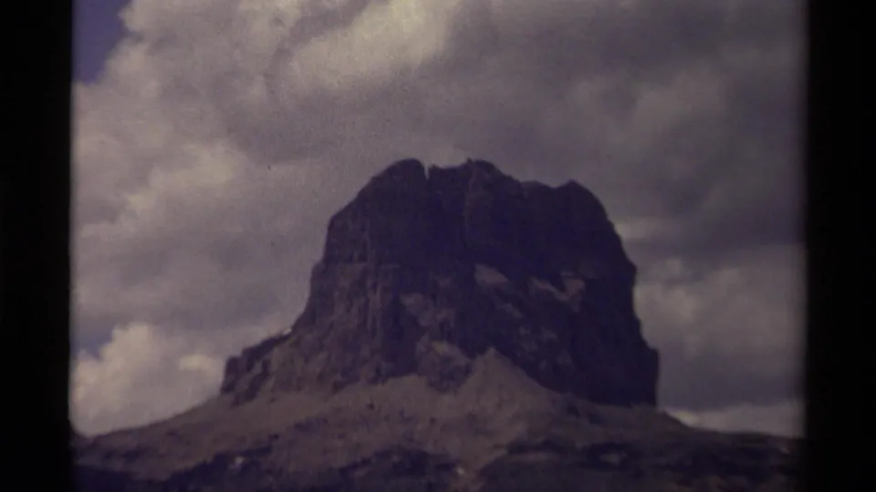 Closer 1979 8mm view of a rugged Canadian mountain face, with cloudy sky and softened home-movie grain.