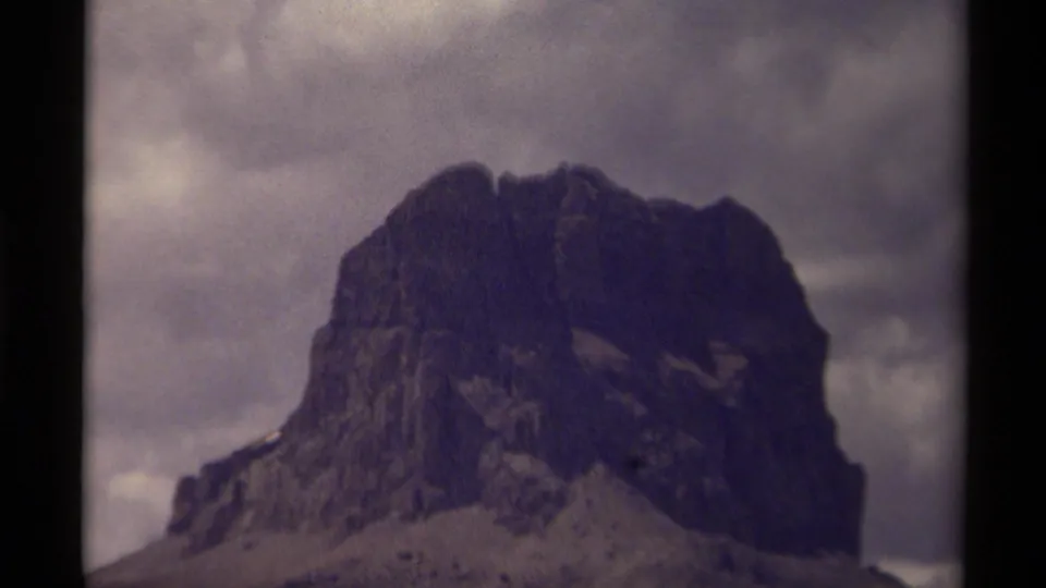 Tight 8mm frame of the Canadian mountain peak, emphasizing the dark rock face, uneven summit, and clouded sky.