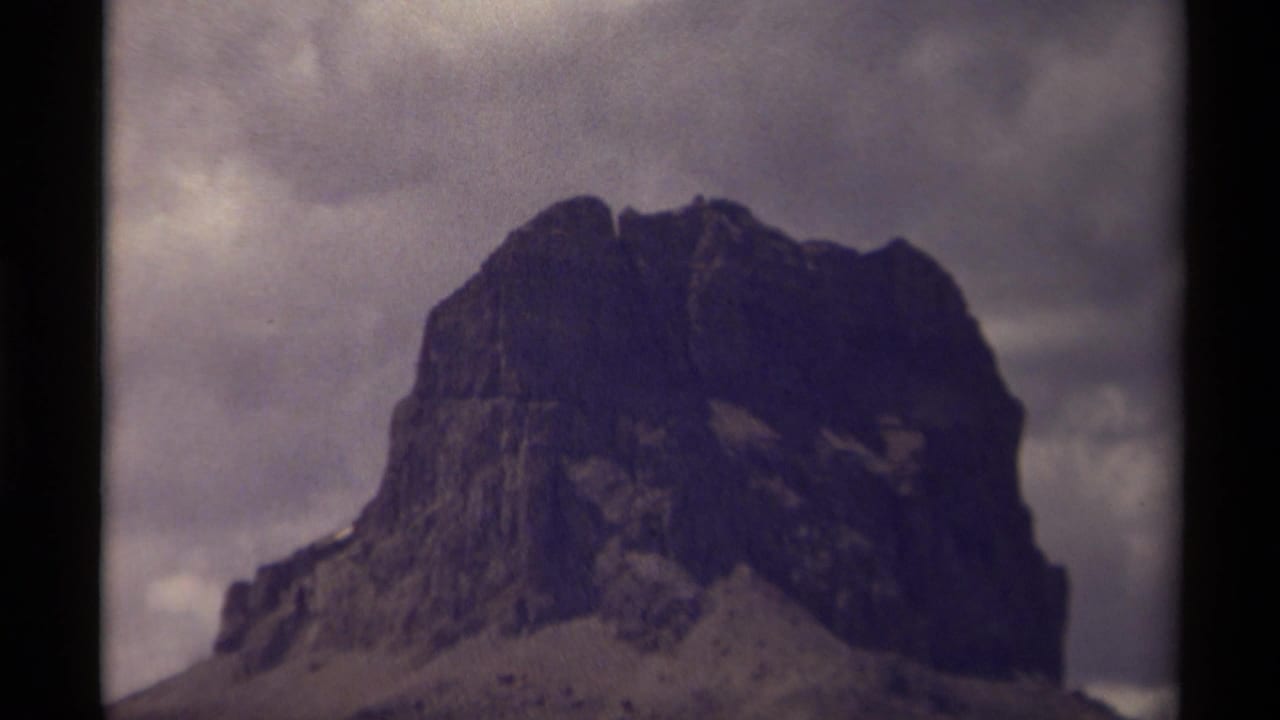 Dark rocky mountain or large rock formation under a cloudy sky.