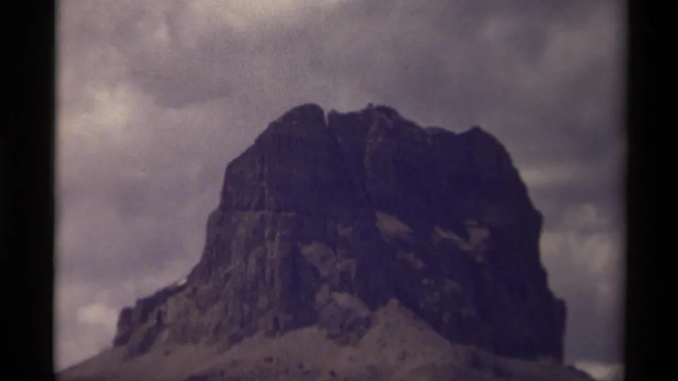 1979 8mm travel footage showing a dark rocky mountain or large rock formation beneath heavy cloud cover.