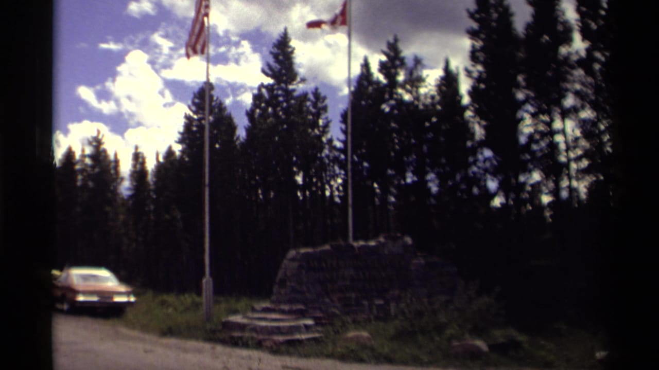 Flags above a rock monument beside a road with trees and a car.