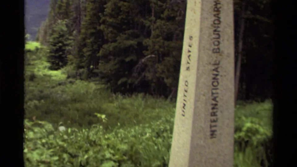 Close view of a United States international boundary monument in a wooded Canada border setting, surrounded by grass and trees.