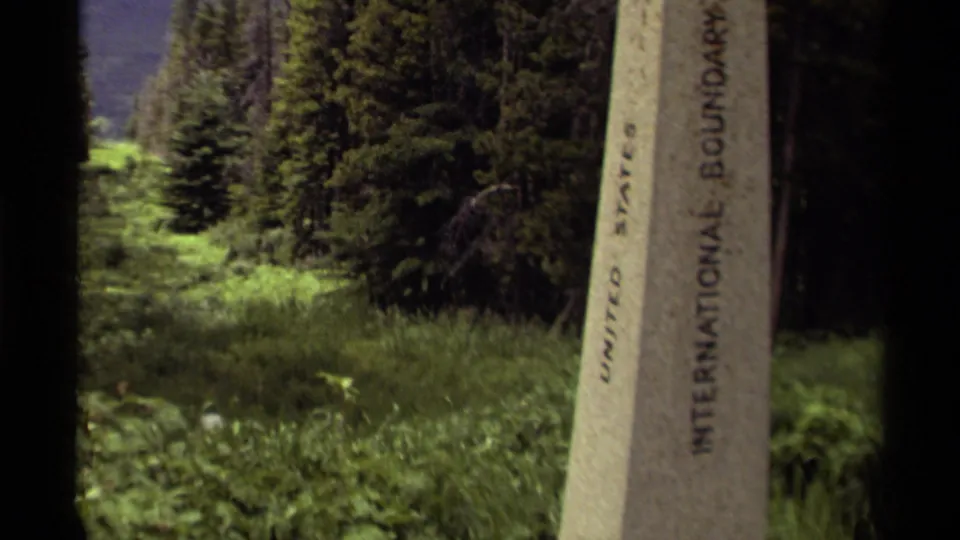 Close 1979 Canada travel shot of the stone international boundary marker, with the inscription partly visible and forest behind it.