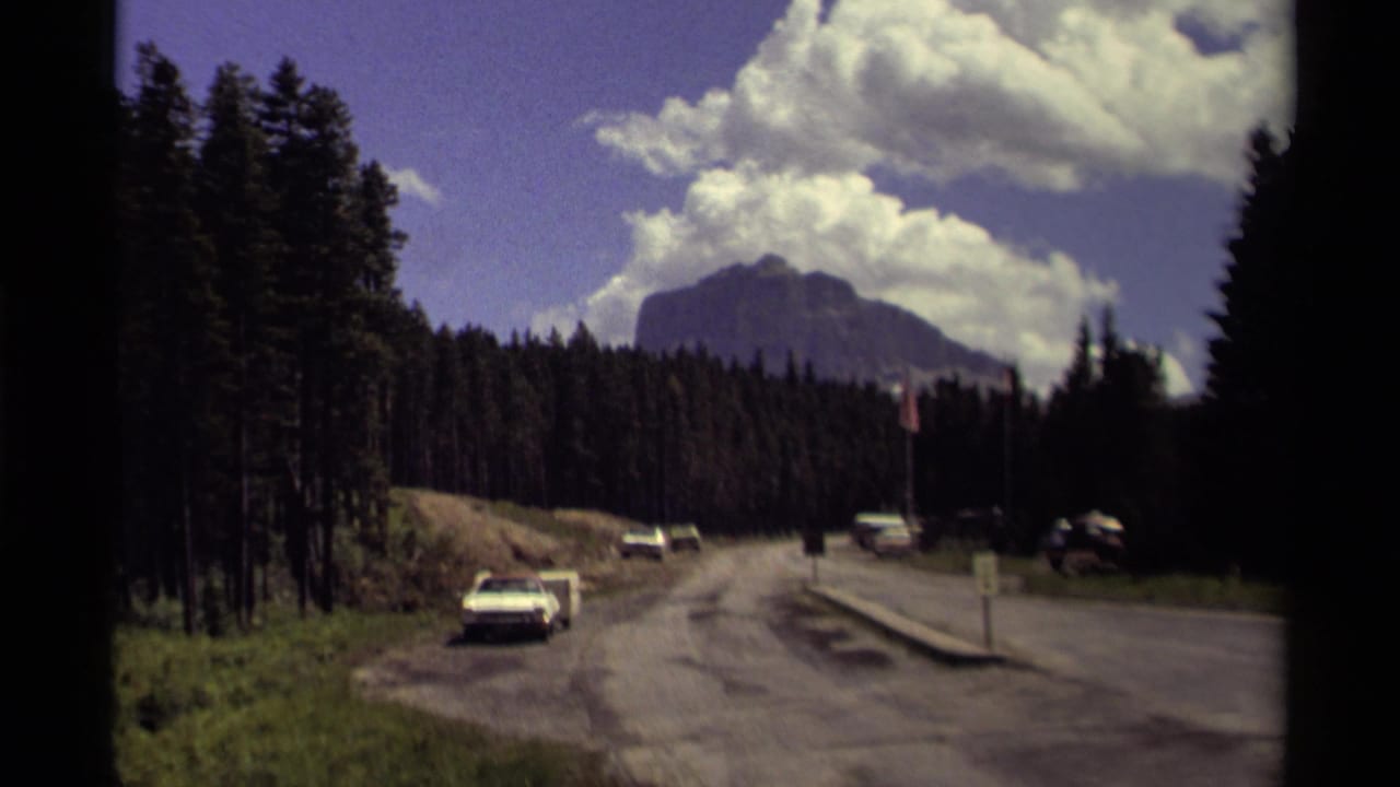 1979 8mm view of a Canadian mountain road with cars passing through forest toward a distant peak.