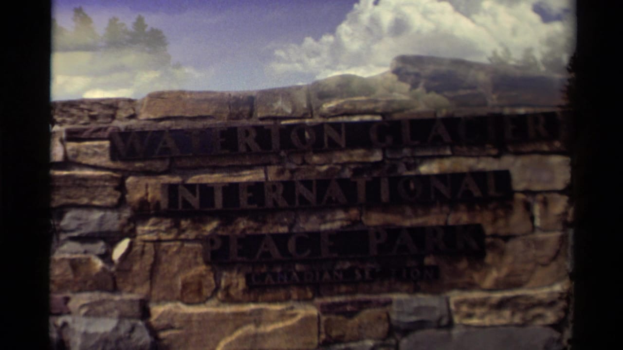 Stone sign reading Waterton Glacier International Peace Park beneath cloudy sky.