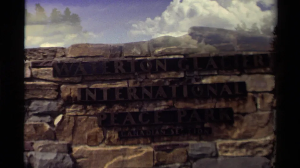 Close view of the stone Waterton Glacier International Peace Park sign, partly dark from exposure.