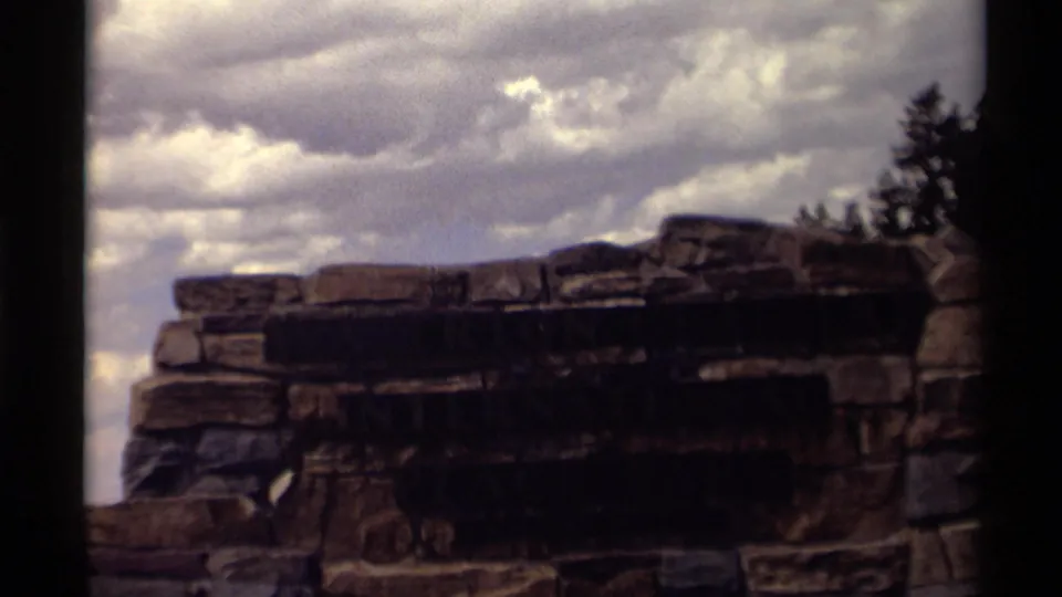 End frame showing a cropped stone park sign against clouds and trees in an 8mm travel shot.
