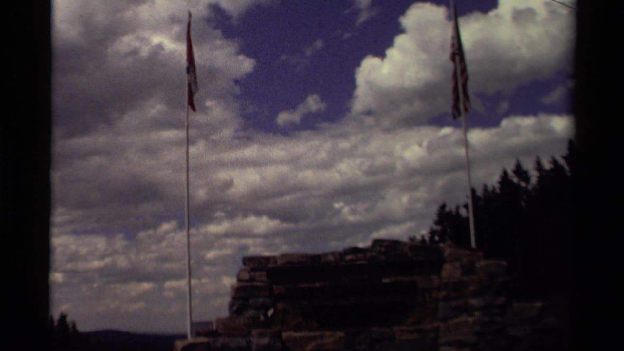 Two flagpoles rise beside a stone structure under a dramatic cloudy sky.