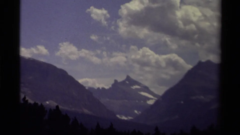 1979 Canadian 8mm view through a mountain pass toward a snow-marked peak, with forest silhouette and clouds across the sky.