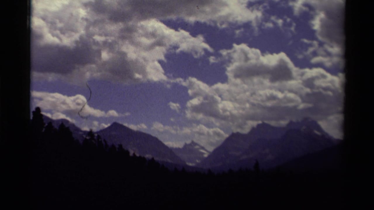 1979 Canada 8mm frame showing silhouetted trees, distant mountain peaks, snow traces, and a textured cloud-filled sky.