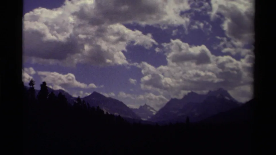 1979 Canada 8mm view of evergreen silhouettes, shadowed mountain forms, small snowfields, and a wide cloud-filled sky.