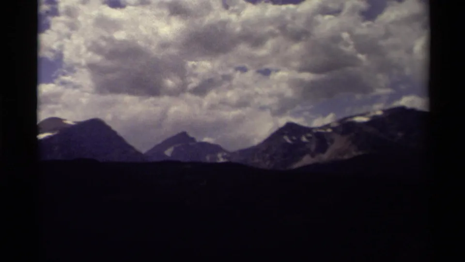 End of the pan shows Canadian mountain slopes and distant peaks under layered clouds in vintage 8mm footage.