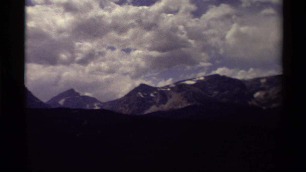 1979 8mm Canada travel footage showing distant snow-dusted mountains under dramatic clouds with dark frame edges.