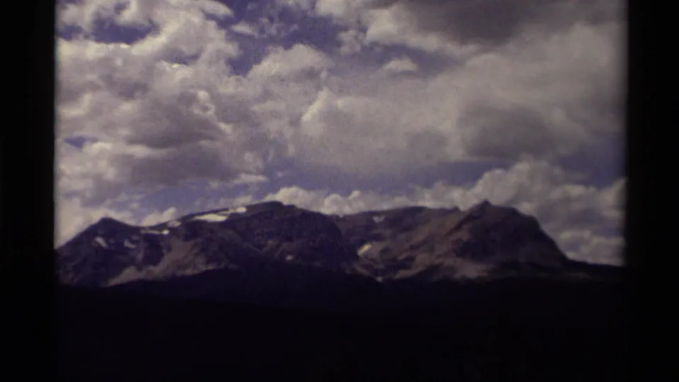 1979 8mm Canada footage of mountains beneath dense cloud formations, with the landscape partly silhouetted at the bottom.