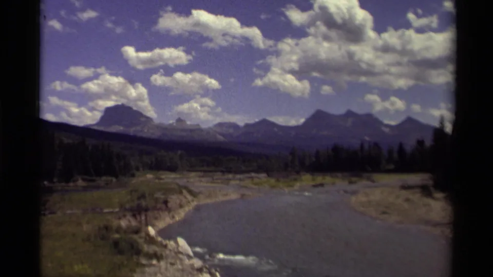1979 Canadian landscape footage showing a river through a valley, evergreen trees, distant mountains, and a partly cloudy sky.