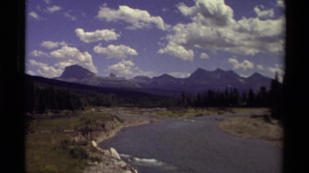 1979 Canadian 8mm frame showing a blue river, forested valley, distant mountains, and scattered white clouds.