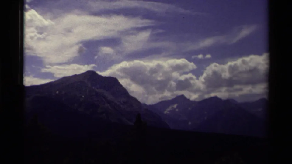 1979 Canadian 8mm frame shifting to darker mountain peaks under broad clouds and blue sky.