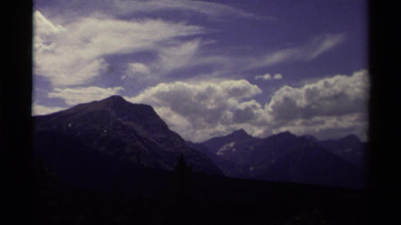 1979 Canadian 8mm view of mountain ridges beneath a bright cloud bank, framed by dark foreground trees and rounded film edges.