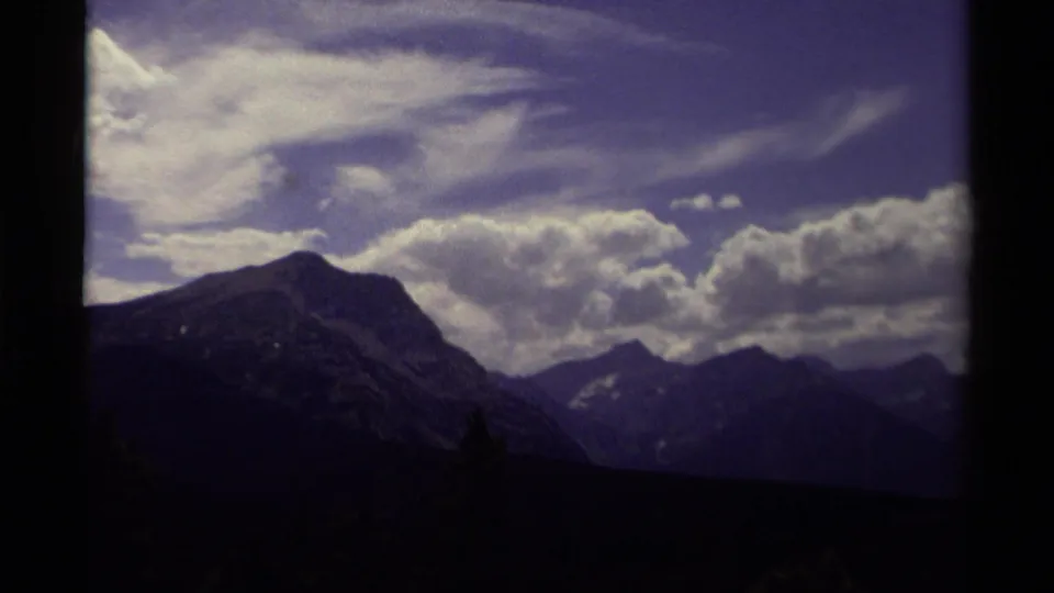 1979 Canadian 8mm view of mountain ridges beneath a bright cloud bank, framed by dark foreground trees and rounded film edges.