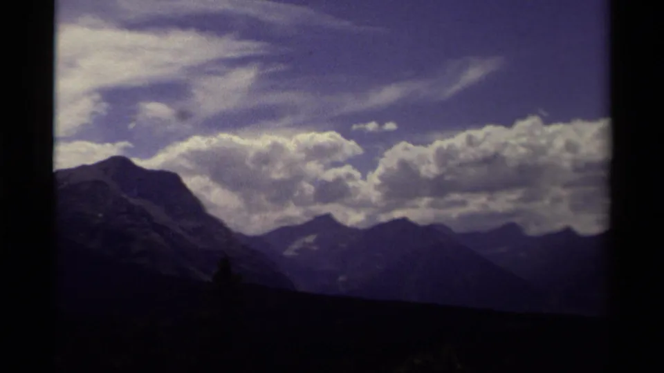 1979 Canadian home-movie frame showing a mountain range below layered white clouds and a blue-purple sky.