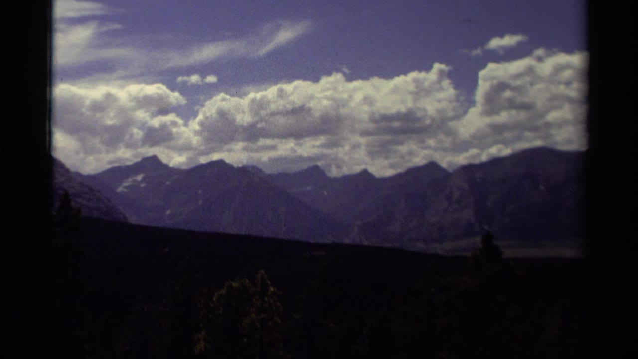 Distant mountain range beneath bright clouds with dark foreground silhouettes and film-frame borders.