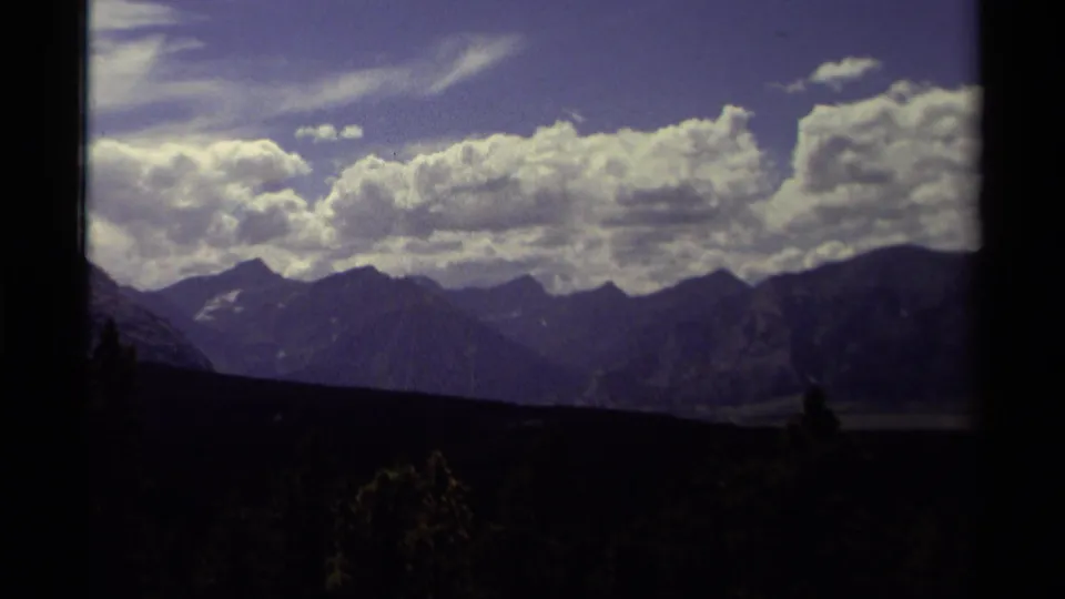 1979 8mm home-movie view in Canada showing distant mountain peaks under a clouded summer sky, framed by dark foreground edges.