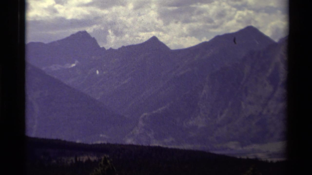 1979 Canadian 8mm home-movie view of shadowed mountain peaks, cloudy sky, and a dark forested foreground.