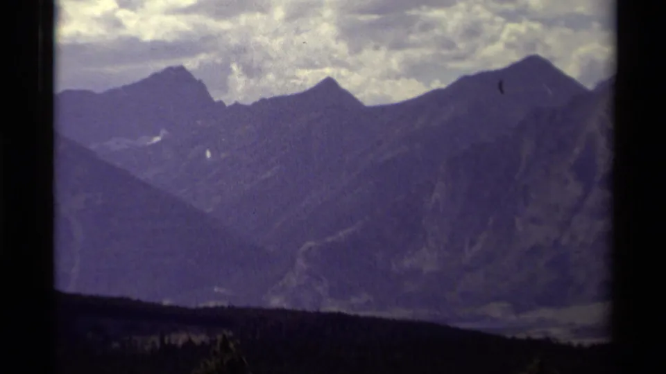 1979 Canadian 8mm home-movie view of shadowed mountain peaks, cloudy sky, and a dark forested foreground.