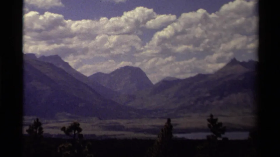 1979 Canadian 8mm home-movie frame of a cloudy mountain valley, dark slopes, low trees, and distant water.