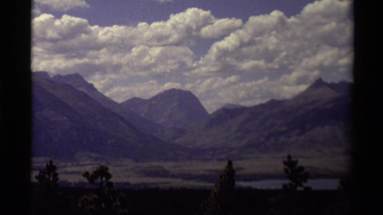 Layered mountain valley beneath large clouds, partly framed by dark vertical edges.