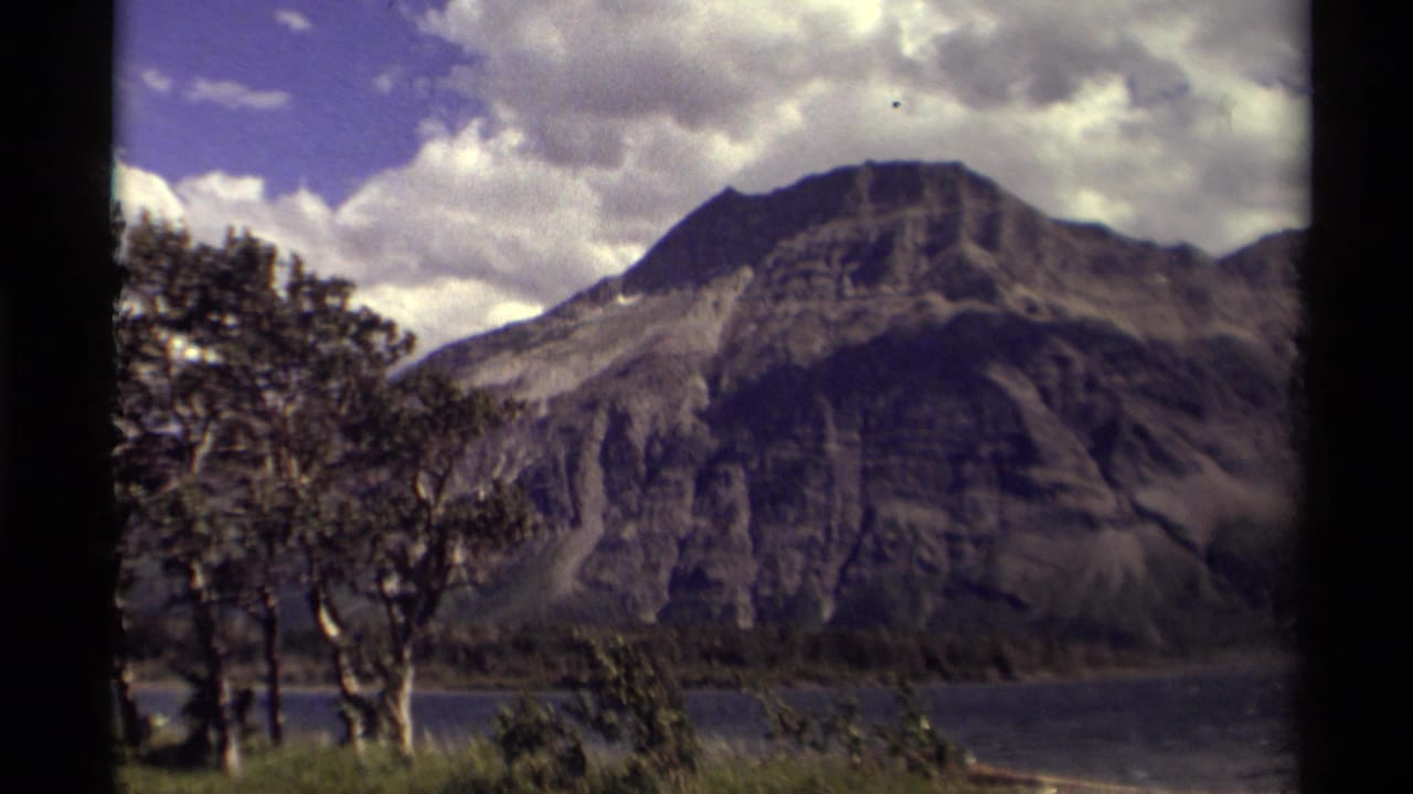 Mountain peak across water, with trees in the foreground and heavy clouds.