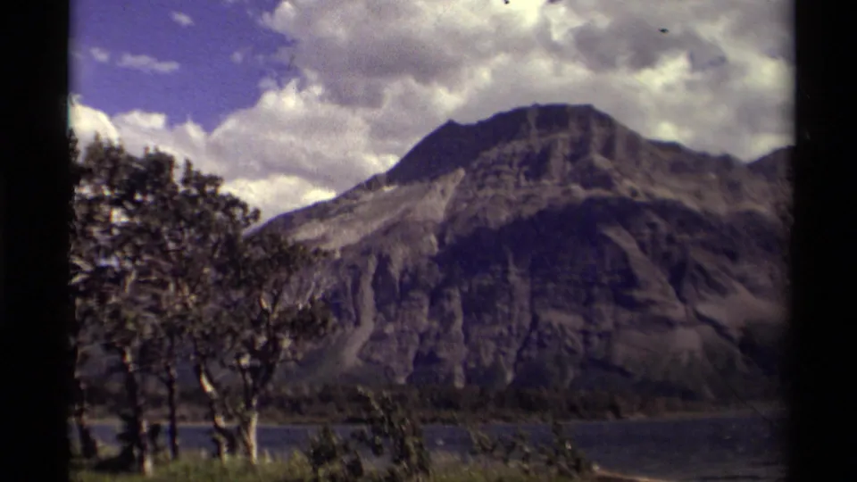 1979 Canadian 8mm frame with a closer view of a rocky mountain above a lake, bordered by trees and cloud cover.