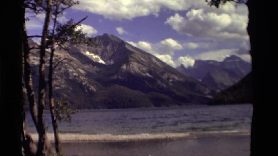 1979 Canadian 8mm frame of mountains rising beyond a lake, with foreground trees and visible small-gauge film borders.