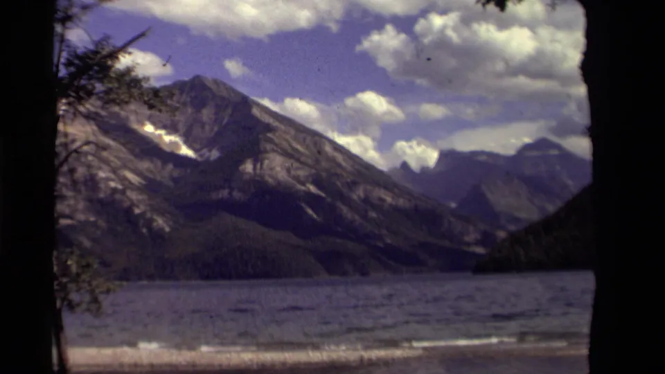The zoom holds on a Canadian mountain lake landscape, with dark trees at the edges and clouds above the peaks.