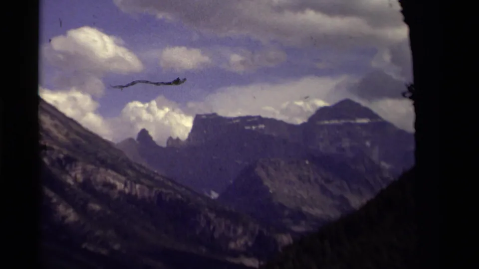 1979 8mm Canada footage showing high mountain peaks and shadowed slopes under a cloud-filled purple-blue sky.